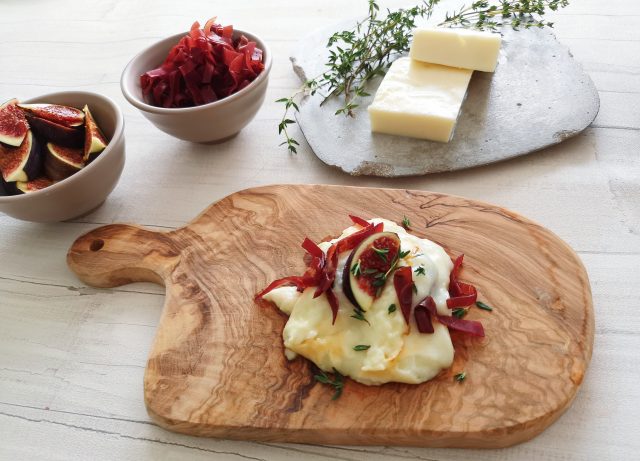 raclette rezept mit brie käse, angerichtet mit Feigen und roten Zwiebeln auf Holzbrett, Käse im Hintergrund